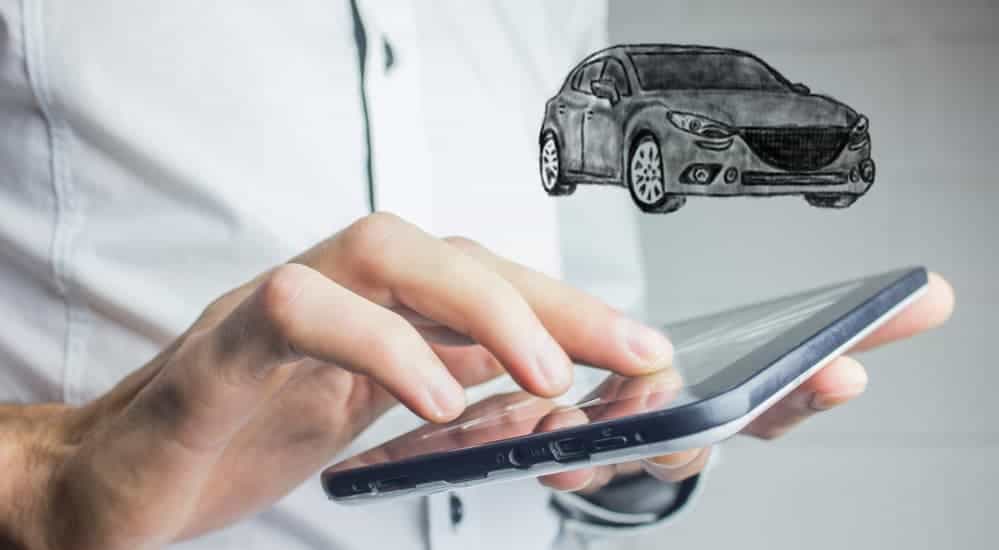 A close up of a man's hands holding a tablet on a site for 'used car lots near me' with a virtual car above is shown.