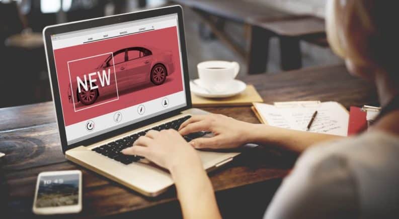 A woman is searching for a new car on an online car dealership on her laptop.