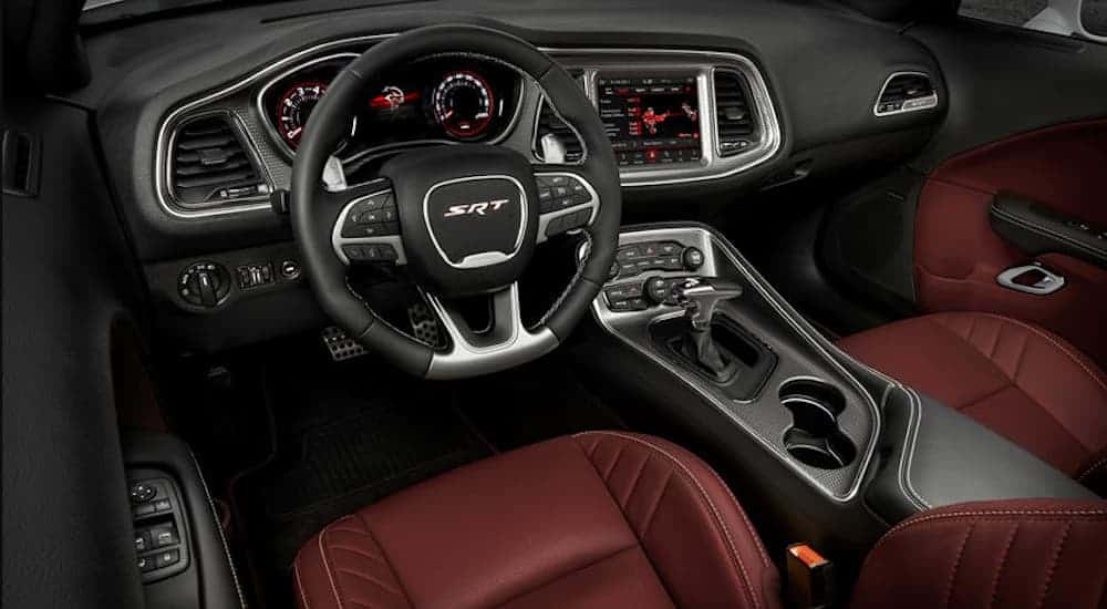 The front red leather interior of a 2019 Challenger Hellcat is shown with an infotainment system and drivers display.