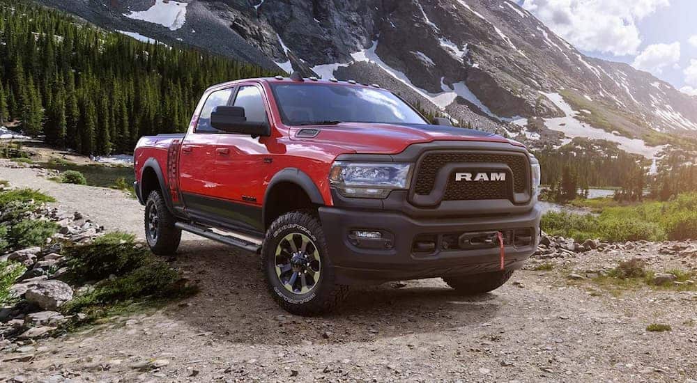 A red and black 2019 Ram 2500 Powerwagon is parked on a dirt road with snow covered mountains in the distance. 