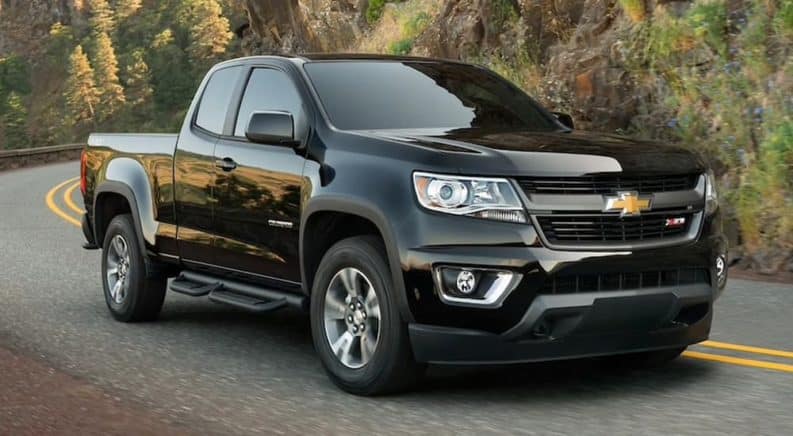 A black 2020 Chevy Colorado is driving on a road past a sharp corner.