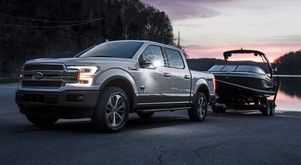 A silver 2020 Ford F-150 is pulling a boat out of a lake at dusk. 