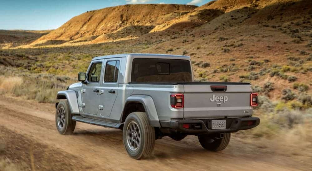 A silver 2020 Jeep Gladiator is driving on a dirt road through the desert.