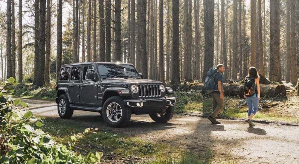 A couple is walking away from a grey 2020 Jeep Wrangler in the woods.
