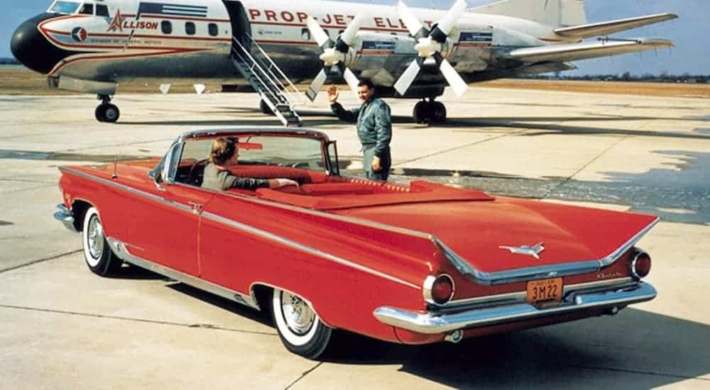 A red 1959 Buick Electra is parked in front of a 1950s plane.