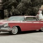 A red 1959 Buick LeSabre is parked with a picnic behind it.