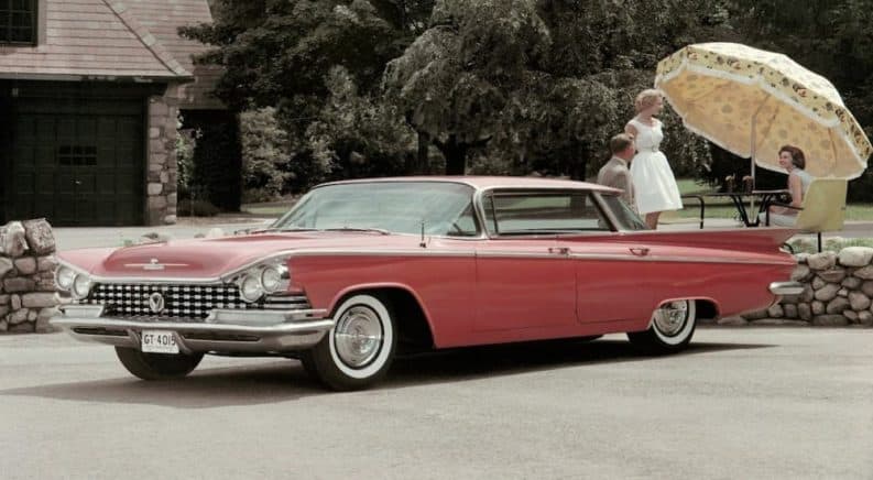 A red 1959 Buick LeSabre is parked with a picnic behind it.
