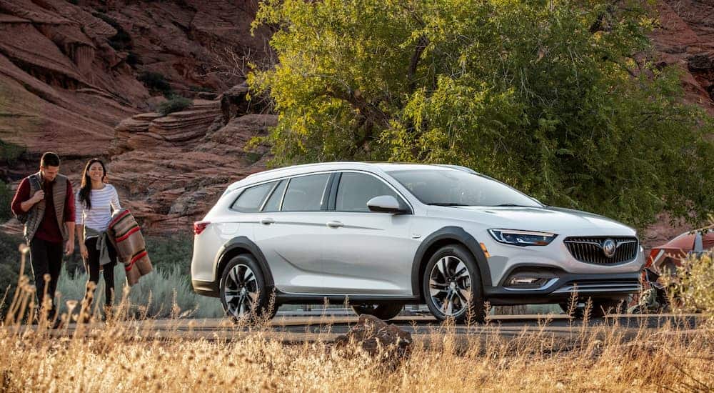 A couple is walking towards a white 2020 Buick Regal TourX after leaving a Buick dealer.