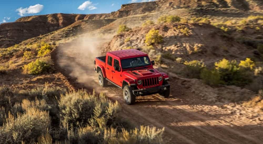 A red 2020 Jeep Gladiator is driving on a dirt road in the desert.