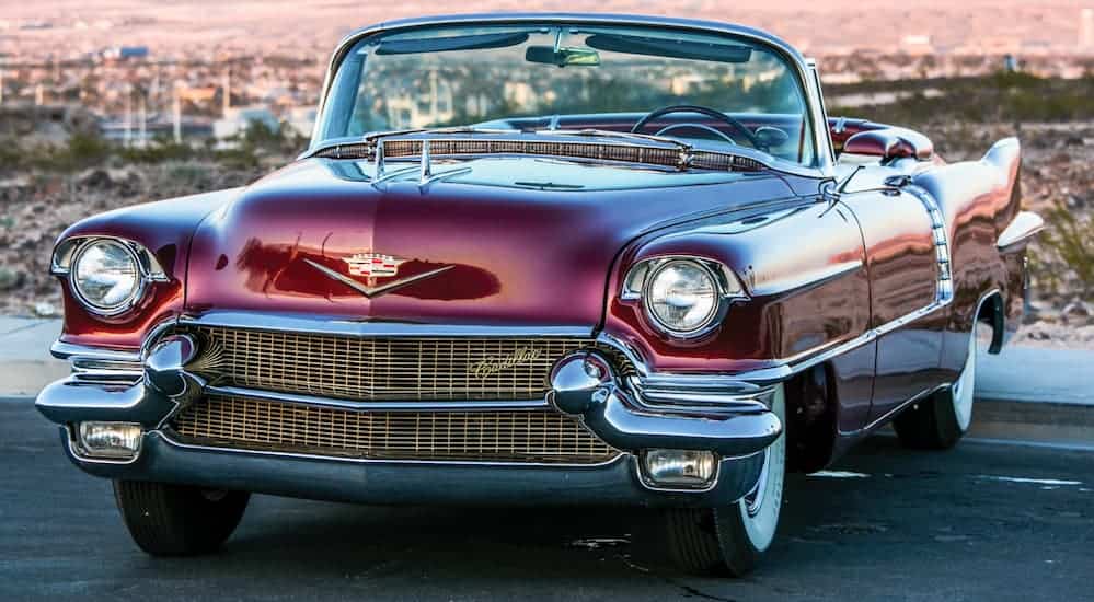 A red 1956 Cadillac Eldorado Biarritz, a car that you could find at classic luxury cars at auction, is parked in a parking lot with mountains in the background.