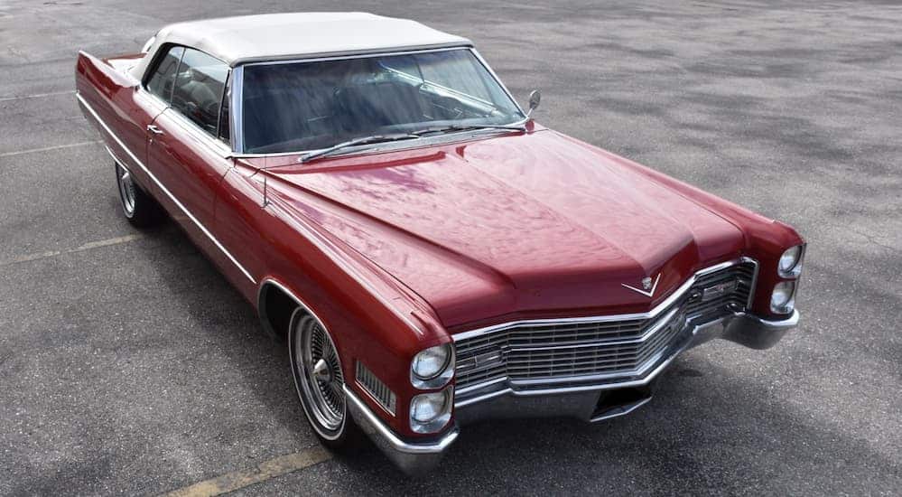 A red 1966 Cadillac Deville is parked in an empty parking lot.