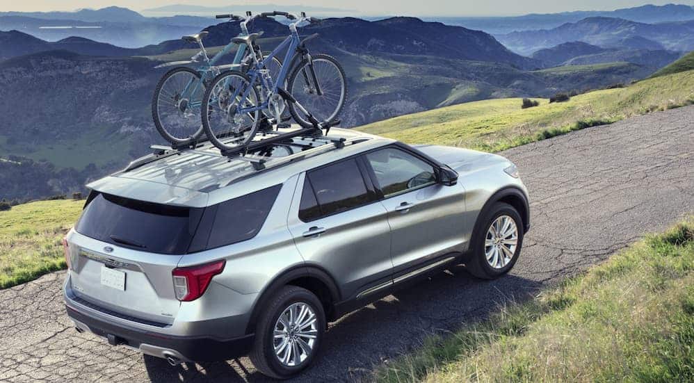 A silver 2020 Ford Explorer is driving up a large mountain with bikes on the roof racks.