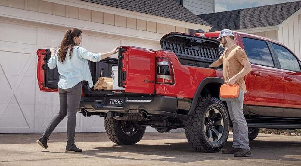 A woman is opening the Multifunction Tailgate of her red 2020 Ram 1500, which is a popular option on many Ram trucks, while parked in front of a house. 