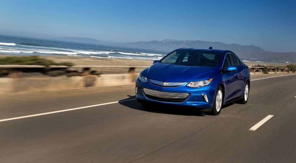 A blue 2017 Chevy Volt, popular among used cars for sale, is driving past the ocean.