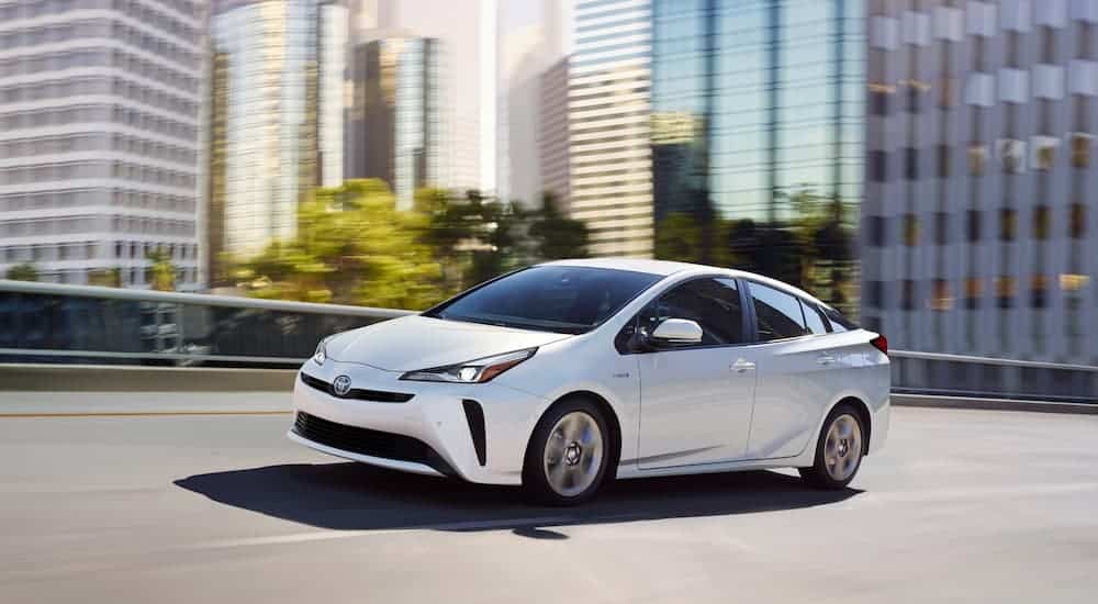 A white 2019 Toyota Prius is driving past city buildings.