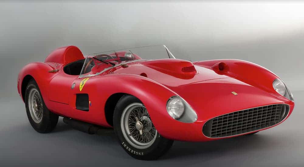 A red 1957 Ferrari 335 S is parked in a white walled garage.