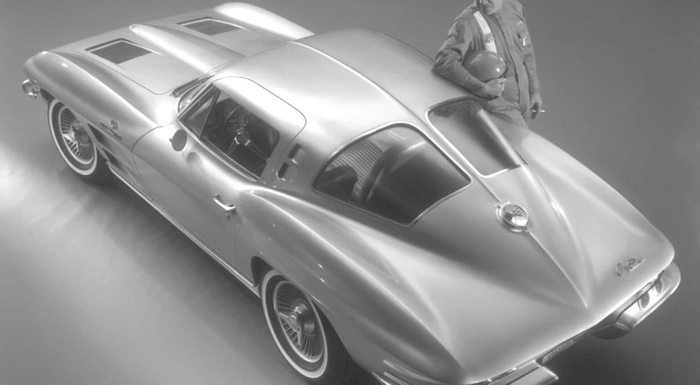 A race car driver is leaning on a 1963 Chevy Corvette, shown in black and white.