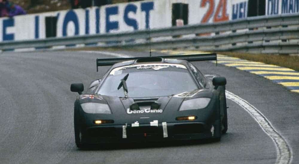 A black 1994 McLaren F1 is driving on a racetrack with grand stands in the distance. 