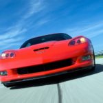 A close up of a red 2011 Chevy Corvette's front end while it's driving on an open highway.