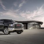 A black 2018 GMC Sierra, which is a popular option among used trucks for sale, is parked in front of a glass house.
