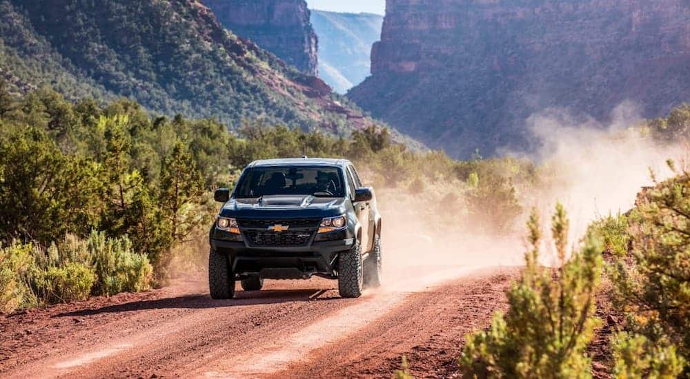 A 2020 Chevy Colorado ZR2 is driving on a dirt road with a dirt cloud forming behind it. 