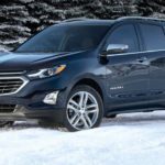 A blue 2020 Chevy Equinox, which wins when comparing the 2020 Chevy Equinox vs 2020 Nissan Rogue, is parked in snow next to snow covered pine trees.