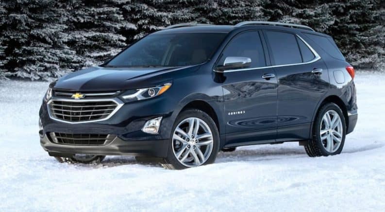 A blue 2020 Chevy Equinox, which wins when comparing the 2020 Chevy Equinox vs 2020 Nissan Rogue, is parked in snow next to snow covered pine trees.