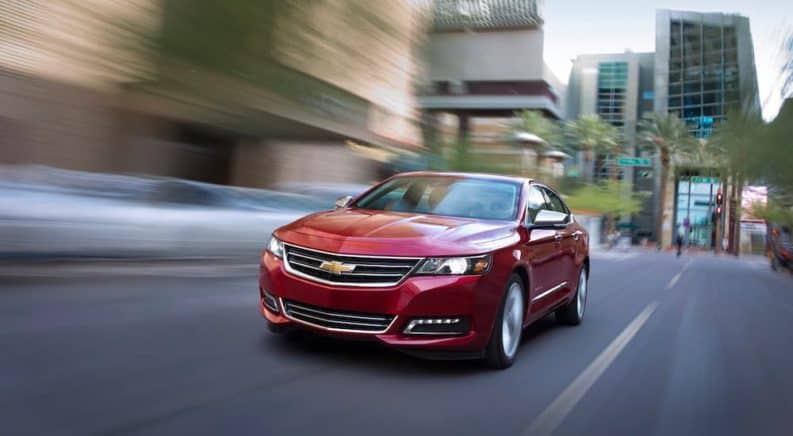 A red 2020 Chevy Impala is driving past blurry buildings.