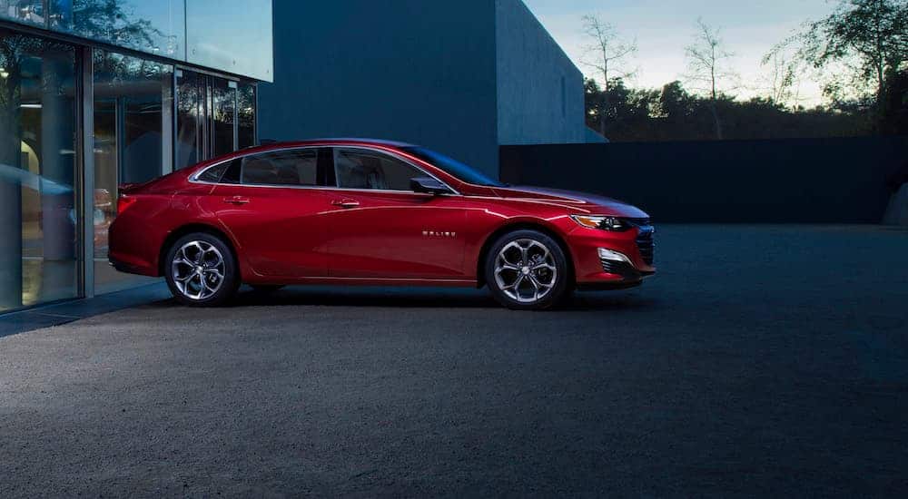 A red 2020 Chevy Malibu is parked in front of a glass building at dusk. 