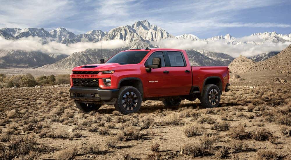 A red 2020 Chevy Silverado 2500HD is parked on dirt with snow covered mountains in the distance. 