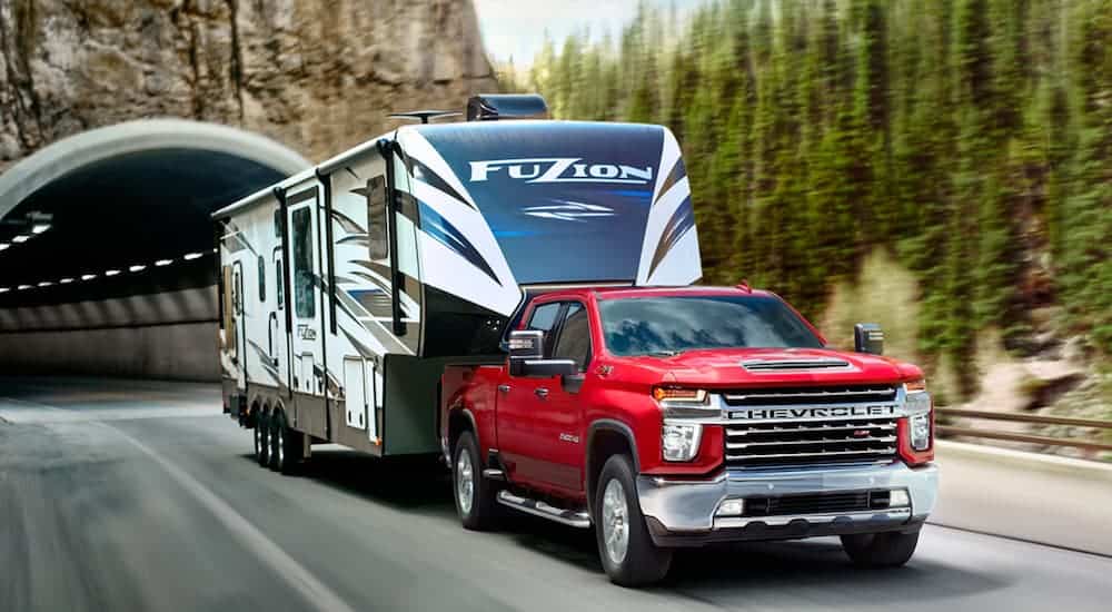 A red 2020 Chevy Silverado 2500HD is towing a large trailer out of a rock tunnel.