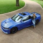 A blue 2020 Dodge Charger is shown from a high angle in a park with a woman leaning against the rear fender.