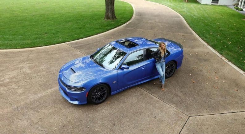 A blue 2020 Dodge Charger is shown from a high angle in a park with a woman leaning against the rear fender.