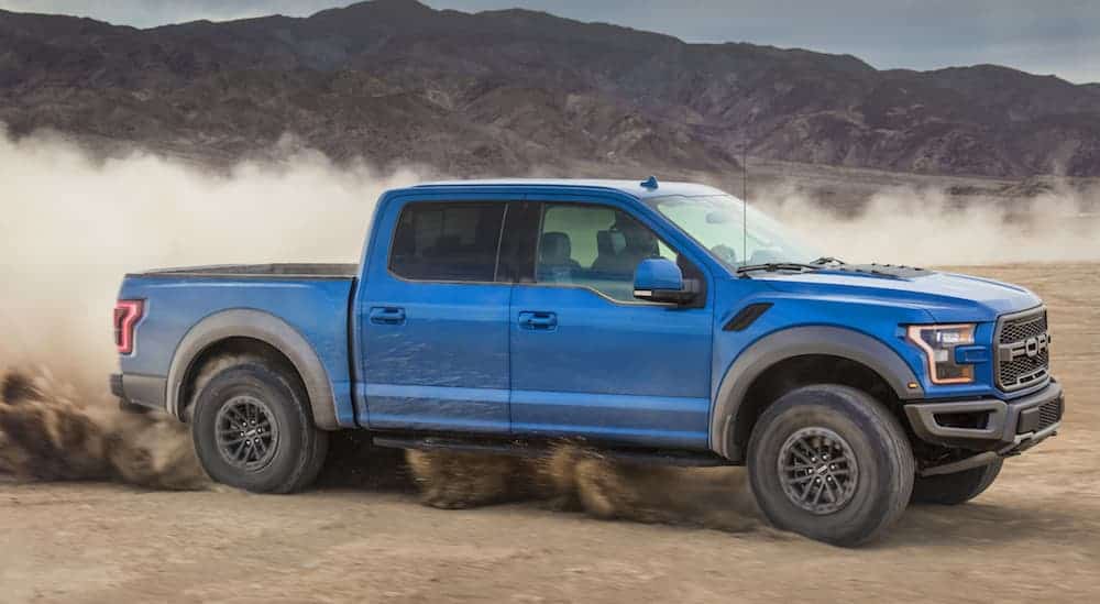 A blue 2020 Ford F-150 Raptor Edition, which wins when comparing the 2020 Ford F-150 vs 2020 Ram 1500, is driving through a dirt pit while a cloud of dirt rises behind it.