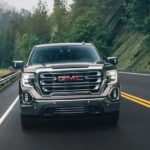 A brown 2020 GMC Sierra 1500 is facing forward while driving on a tree lined road next to a river.