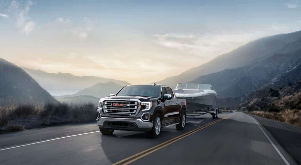 A black 2020 GMC Sierra 1500, which wins when comparing the 2020 GMC Sierra 1500 vs 2020 Ford F-150, is towing a large boat with mountains in the distance. 