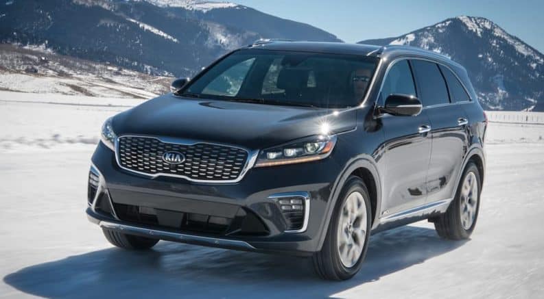 A grey 2020 Kia Sorento is driving on a snow covered road with snow covered mountains in the distance.