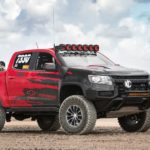 A red and black lifted 2021 Chevy Colorado is parked on dirt.