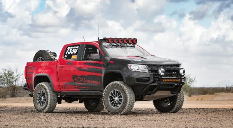 A red and black lifted 2021 Chevy Colorado is parked on dirt.