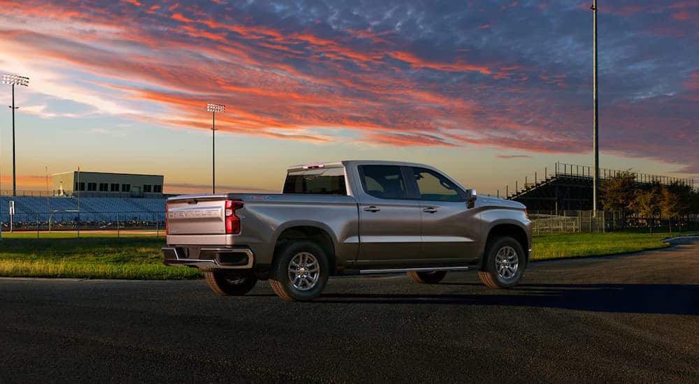 A grey 2021 Chevy Silverado 1500 is shown from the side with a football field in the background.