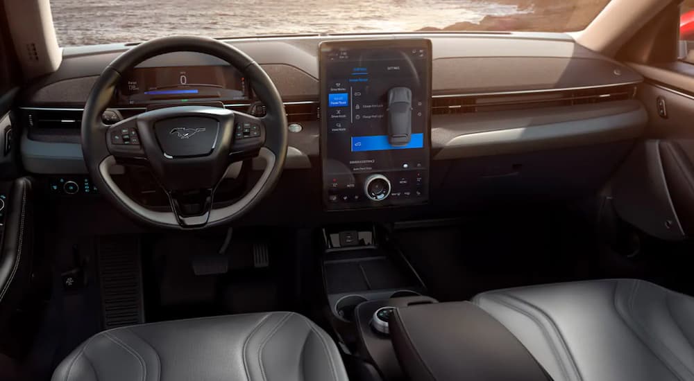 The front black leather interior of a 2021 Ford Mustang Mach-E is shown with a large touchscreen. 