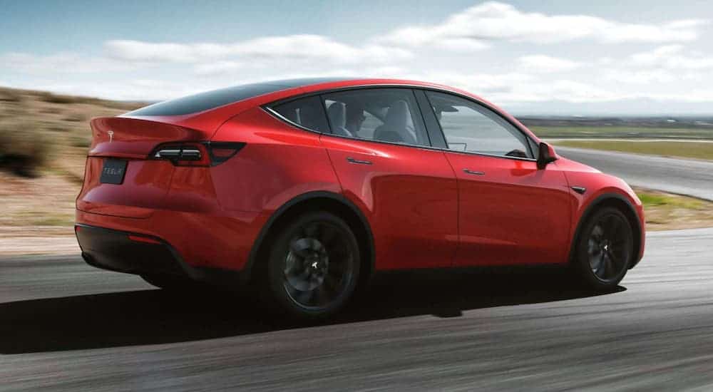 A red Tesla Model Y is driving around a corner on a curvy road. 