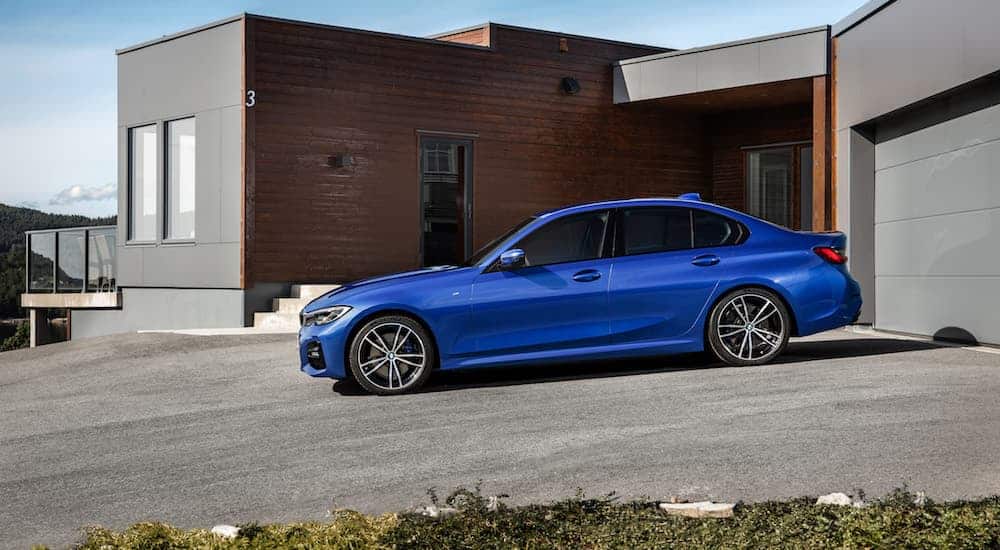 A blue 2019 BMW 3 Series is parked in front of a grey house.