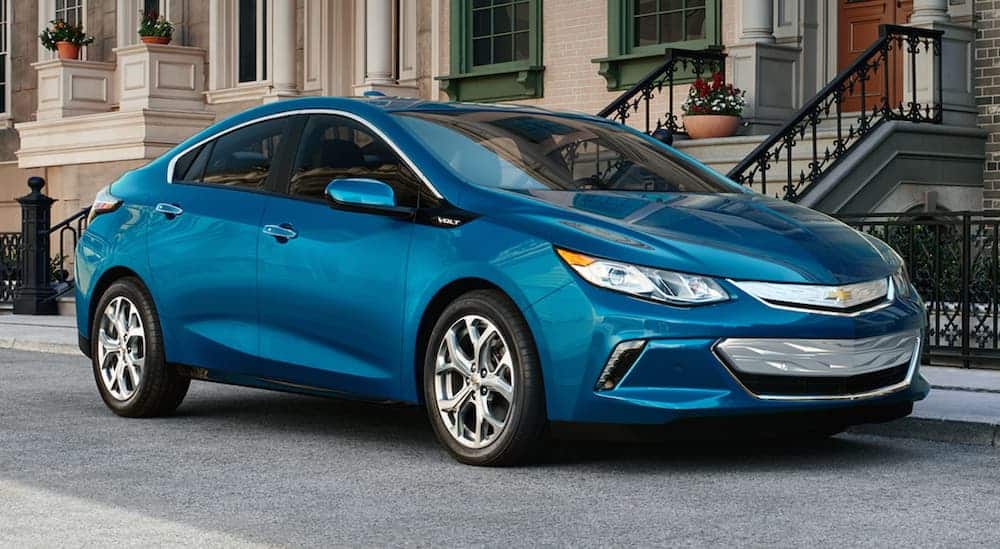 A blue 2019 Chevy Volt is parked in front of a brick apartment building.