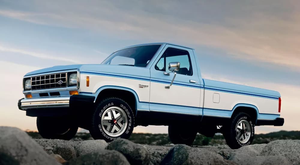 A blue and white 1983 Ford Ranger is parked on rocks at dusk. 