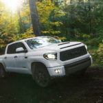 A white 2020 Toyota Tundra is driving through a mud puddle in the middle of the woods.