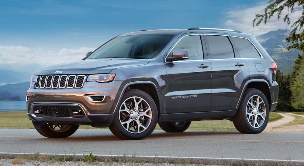 A grey 2018 Jeep Grand Cherokee, which is a popular a option among used car dealerships, is parked on a road next to a grassy field. 