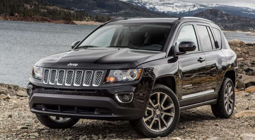A black 2016 Jeep Compass is parked next to a large lake with mountains behind it. 