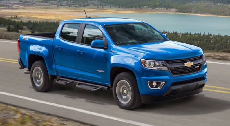 A blue 2020 Chevy Colorado, which wins when comparing the 2020 Chevy Colorado vs 2020 Ford Ranger, is driving on a grass lined road next to a lake.