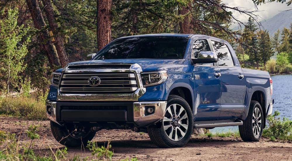 A blue 2020 Toyota Tundra is parked on a dirt trail next to a lake on a sunny day.